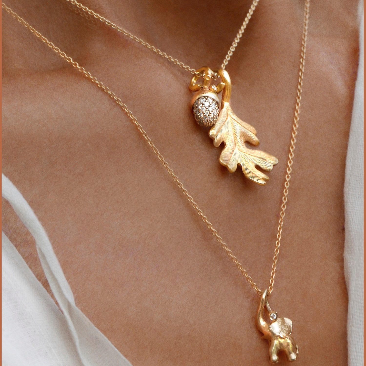 Gold necklace with oak leaf and diamomnd set acorn pendant layered with elephant pendant on a person's neck