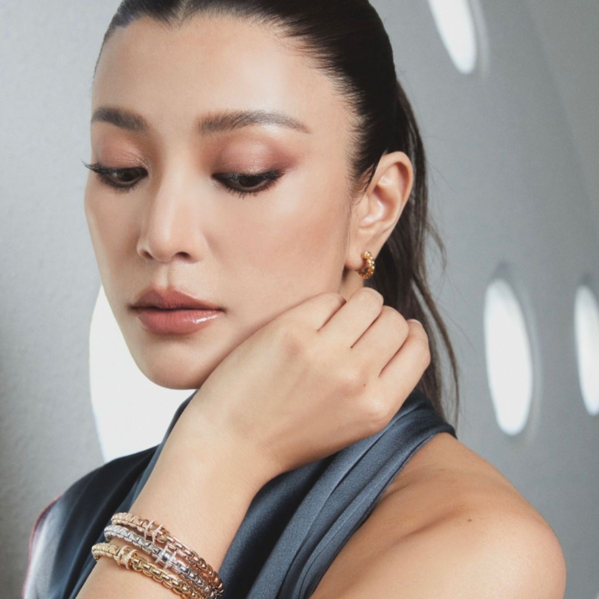 A close-up of a woman wearing Fope Eaka concave diamond edge bracelets including a small fope gold hoop earring 