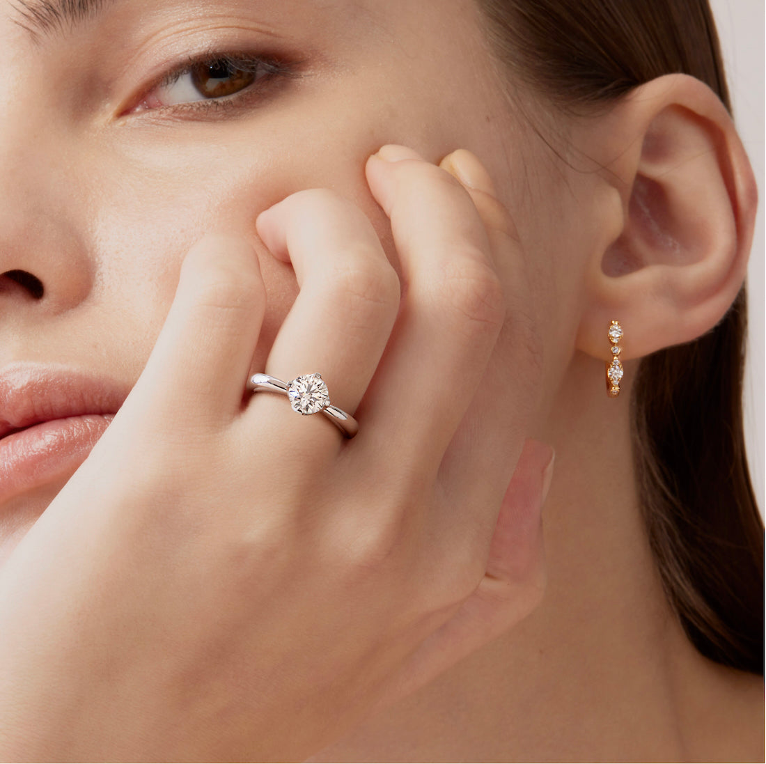 close up of a woman wearing hearts on fire diamond solitaire ring and bezel regal diamond huggie hoop earrings